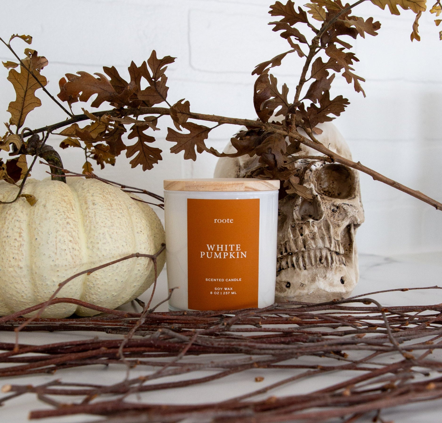 White pumpkin candle with decorative skull and branches on a white surface
